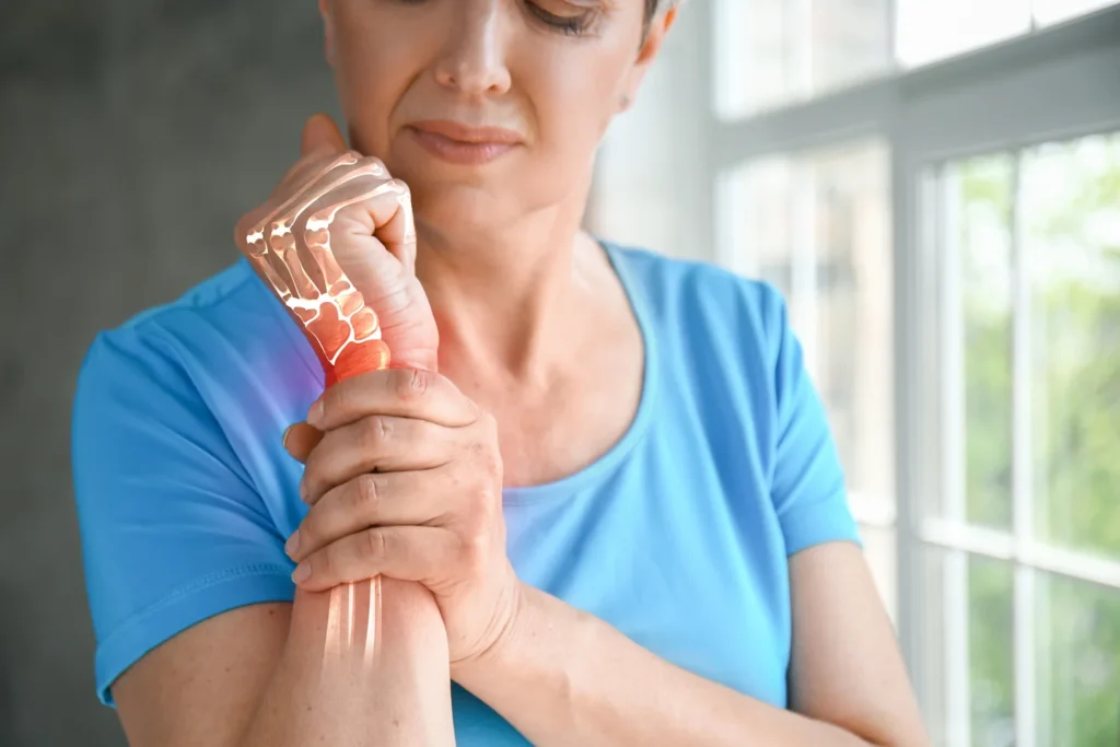 Mulher na menopausa segurando o punho com expressão de dor, representando osteoporose e fragilidade óssea.